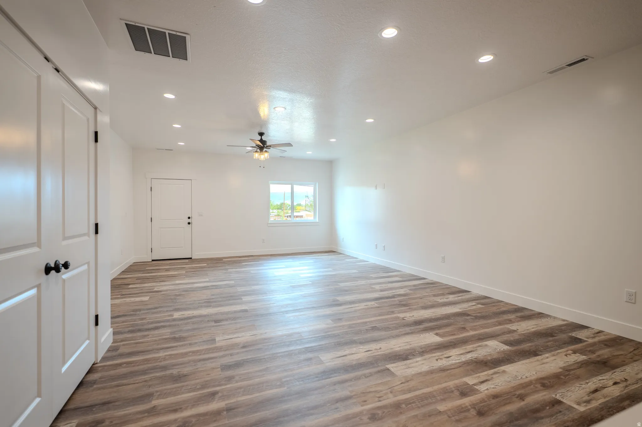 Spacious room featuring wood-finish flooring, recessed lighting, and a ceiling fan