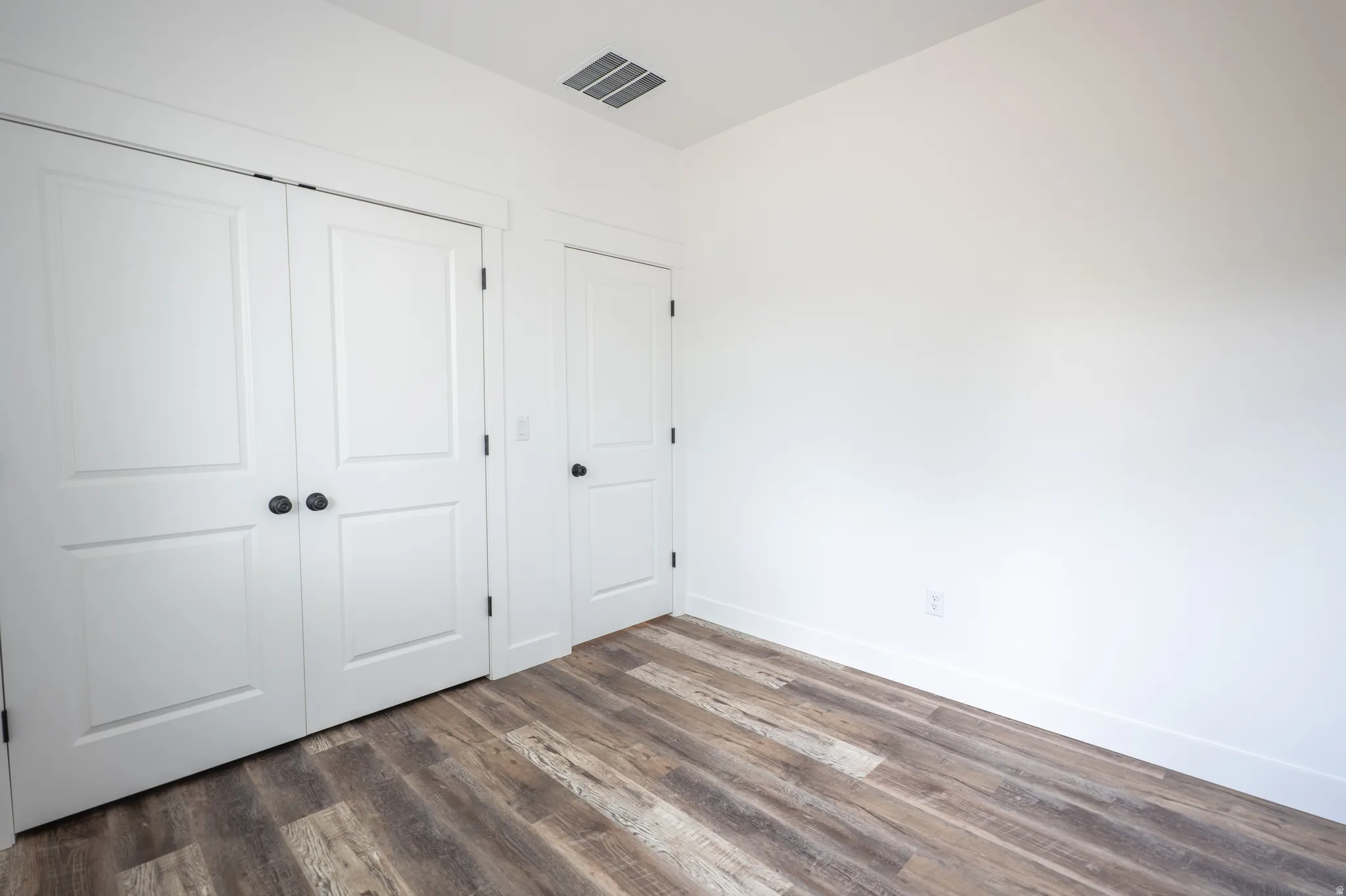 Room featuring wood-finish flooring, crisp white walls, and a recessed ceiling vent