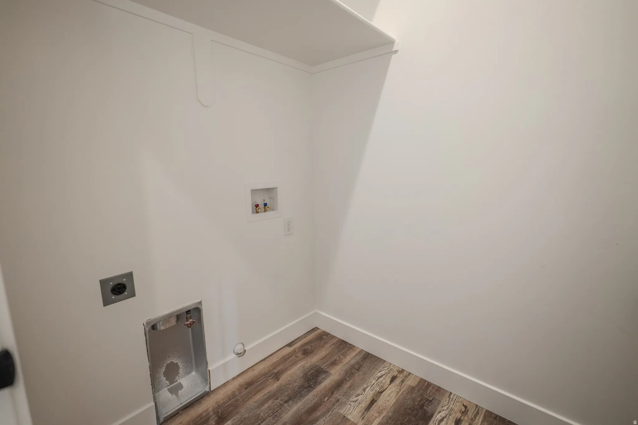 Dedicated utility space featuring wood-finish flooring, white walls, and a built-in shelf