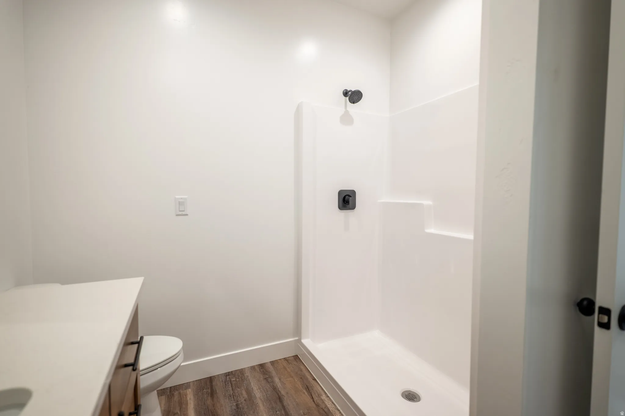 Bathroom featuring a white shower stall with matte black fixtures, a contemporary vanity with a light-colored countertop, and wood-finish flooring