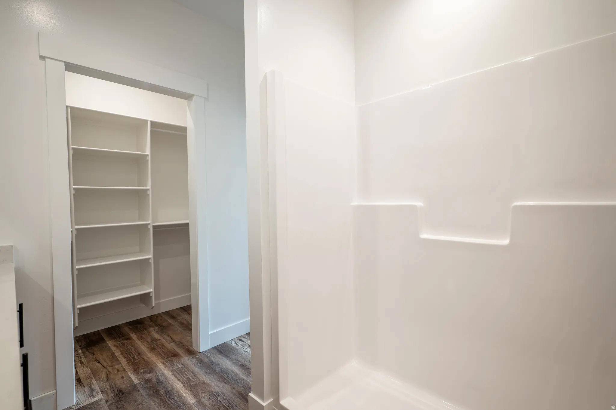 Walk-in closet with extensive white shelving, wood-finish flooring, and a crisp white shower surround with integrated ledges