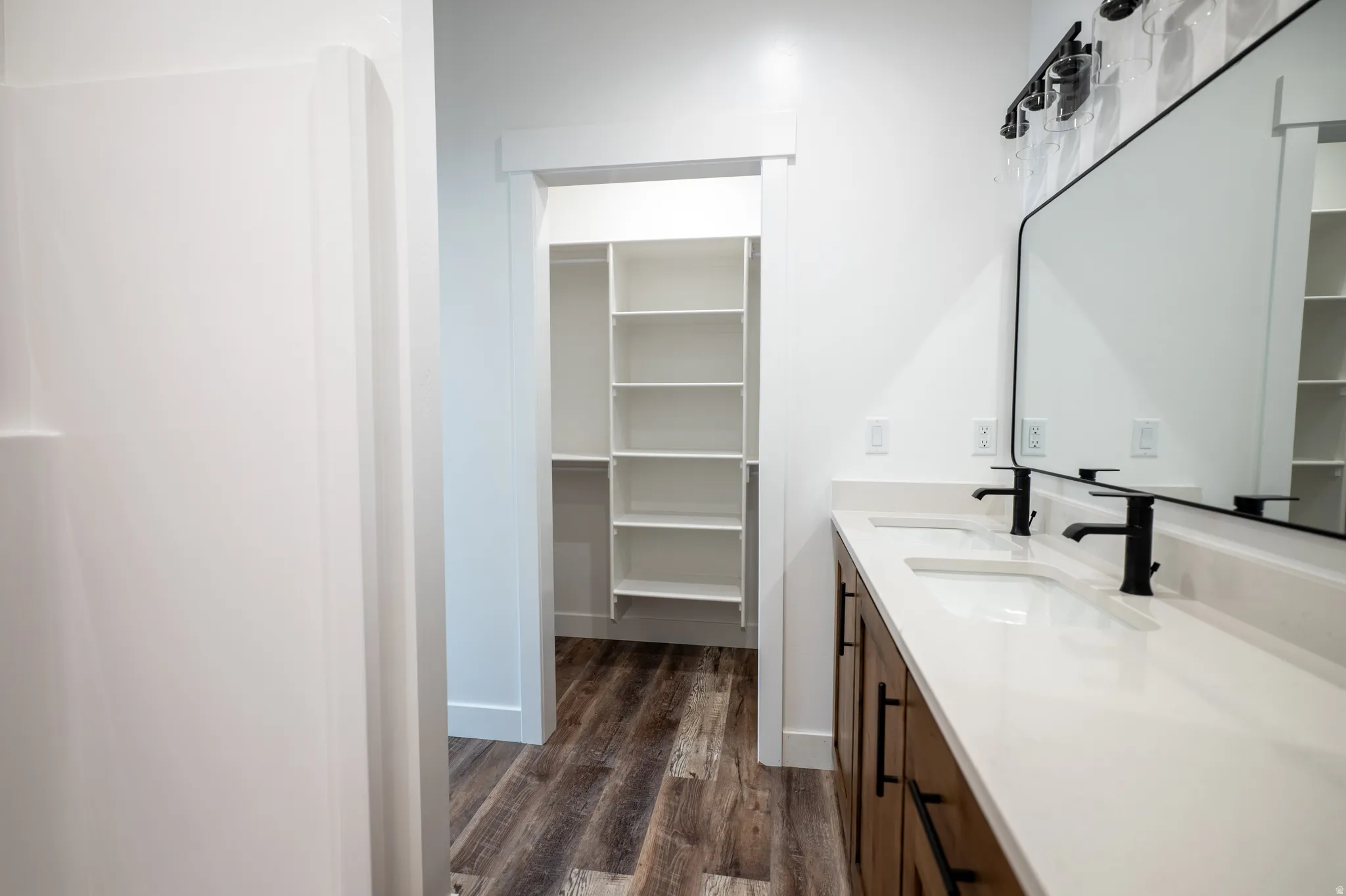Bathroom featuring a double vanity with wood-finish cabinetry, white countertop, and matte black fixtures