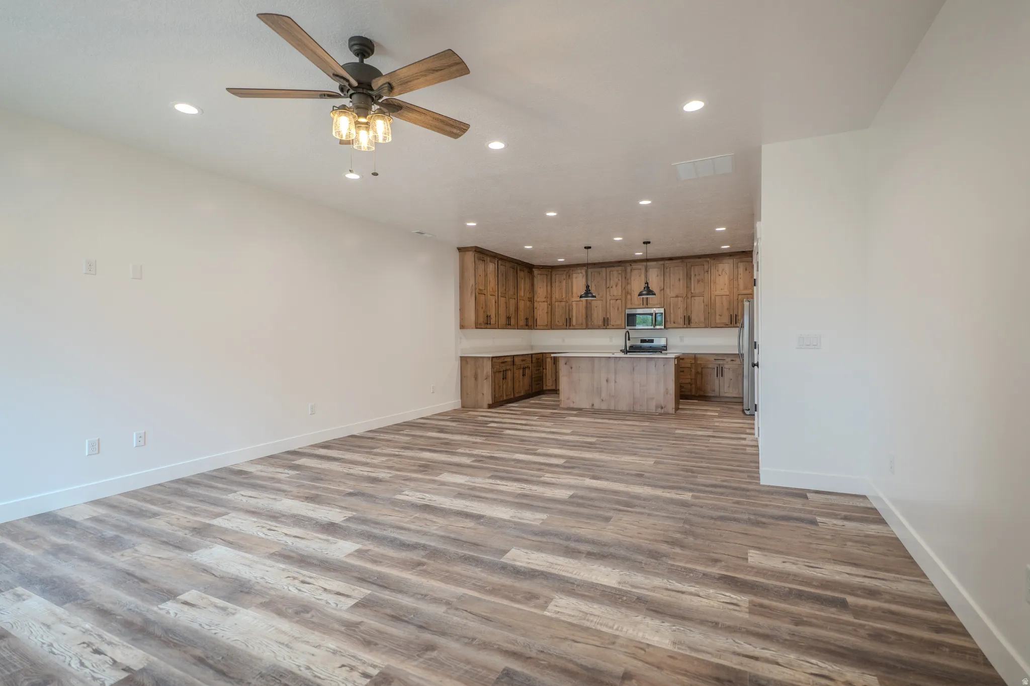 Open-concept living area featuring wood-finish flooring, a ceiling fan with integrated lighting, and recessed ceiling lights