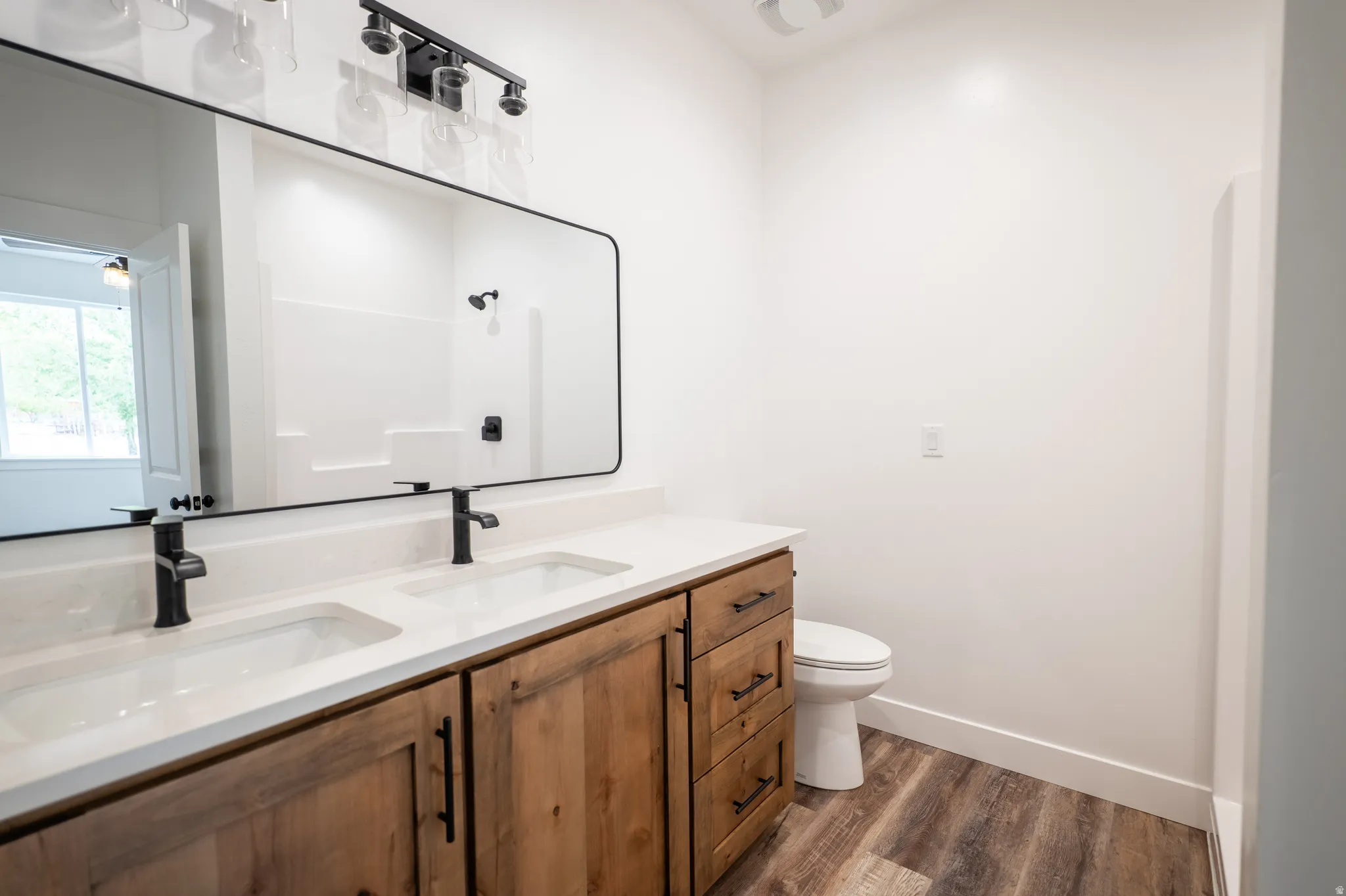 Double vanity featuring wood-finish cabinetry, white countertops, and matte black fixtures