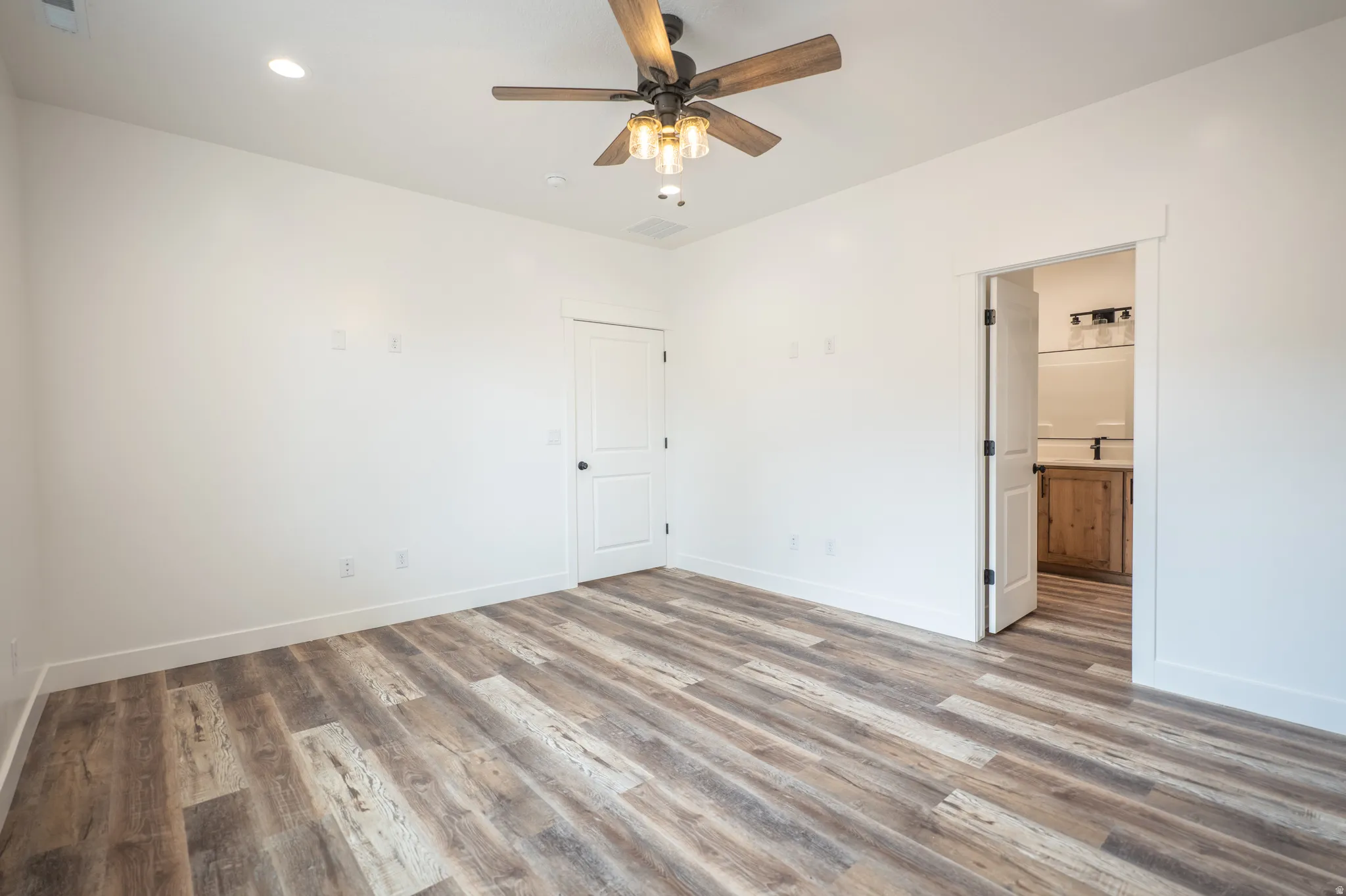 Spacious room featuring wood-finish flooring, a ceiling fan with integrated lighting, recessed lighting, and a white interior door