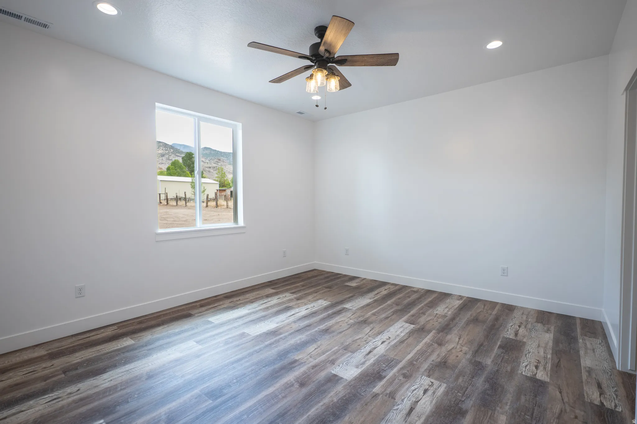 Spacious interior featuring wood-finish flooring, white walls, and a ceiling fan with integrated lighting