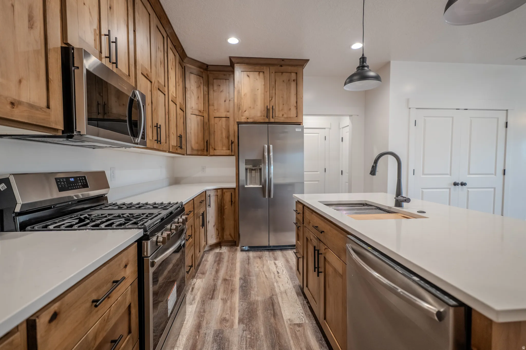 Kitchen featuring wood cabinetry, light-toned countertops, stainless steel appliances, and wood-finish flooring