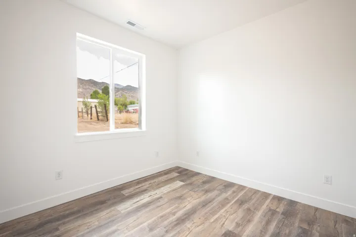 Room featuring wood-finish flooring, white baseboards, a white window frame, and neutral white walls