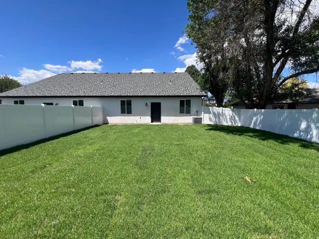Expansive rear yard featuring green lawn, privacy fencing, and a rear exterior with a dark door