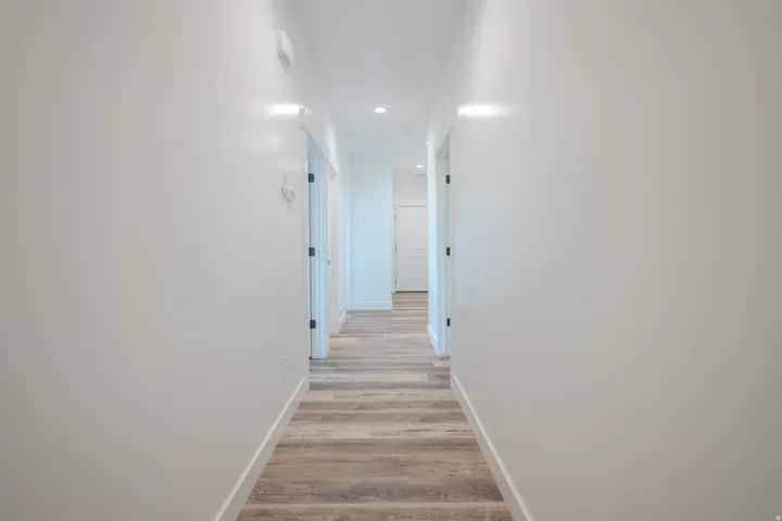 Hallway with wood-finish flooring, recessed lighting, white walls, and multiple panel doors