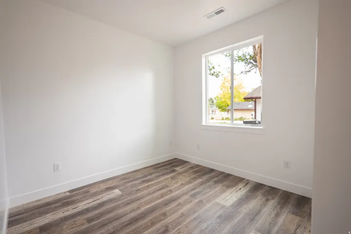 Room featuring wood-finish flooring, white walls, and a white-framed window