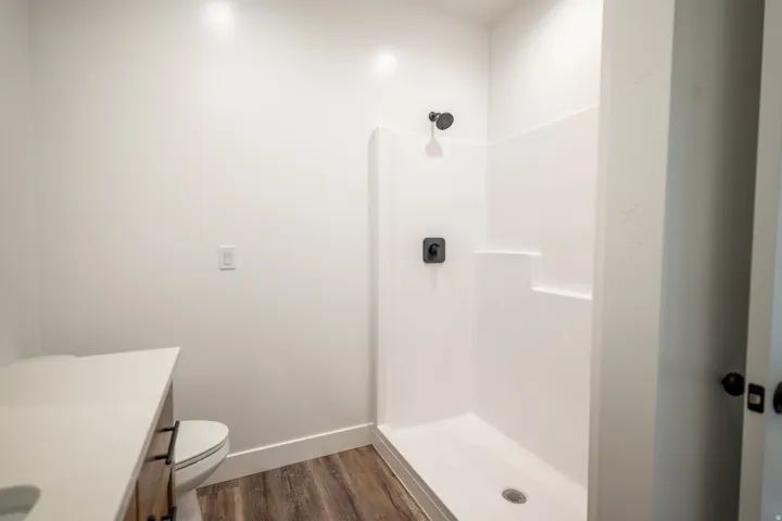 Bathroom featuring a white shower stall with matte black fixtures, a contemporary vanity with a light-colored countertop, and wood-finish flooring