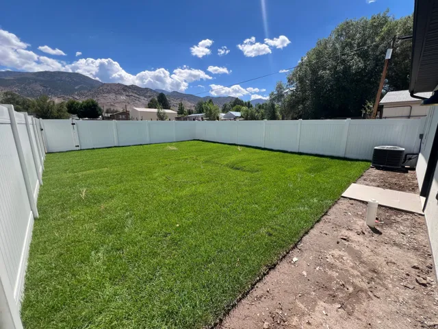 Expansive backyard featuring a lush lawn, privacy fencing, and an exterior HVAC unit