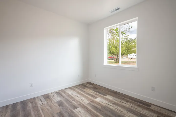 Bright room featuring wood-finish flooring, white baseboards, a large window, and white walls