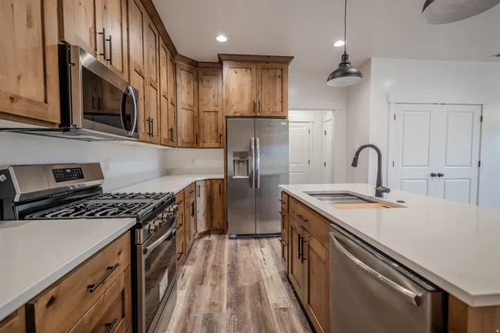 Kitchen featuring wood cabinetry, light-toned countertops, stainless steel appliances, and wood-finish flooring