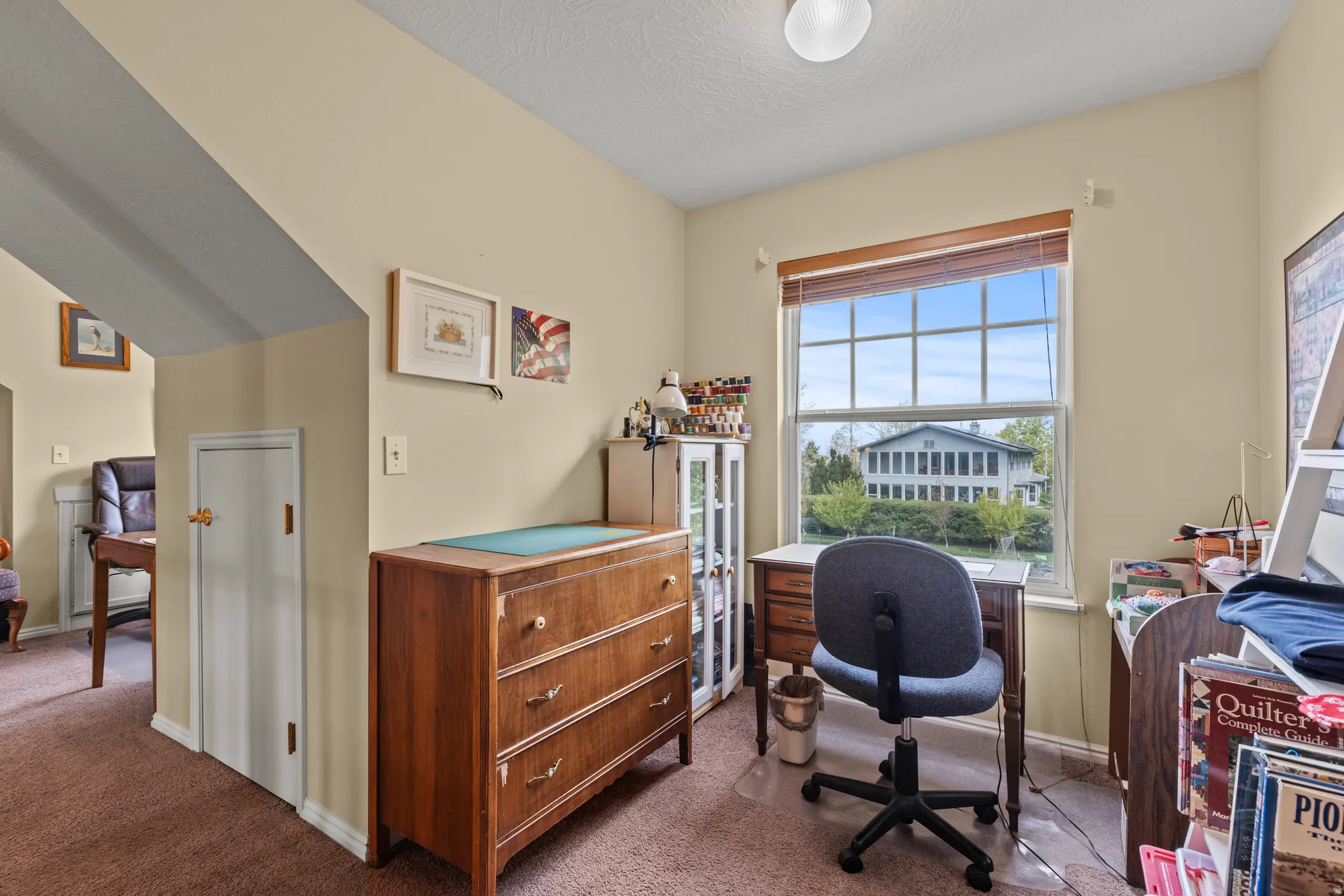 Room featuring a window with a wood-finish blind overlooking exterior landscaping, light beige wall paint, and brown carpeting