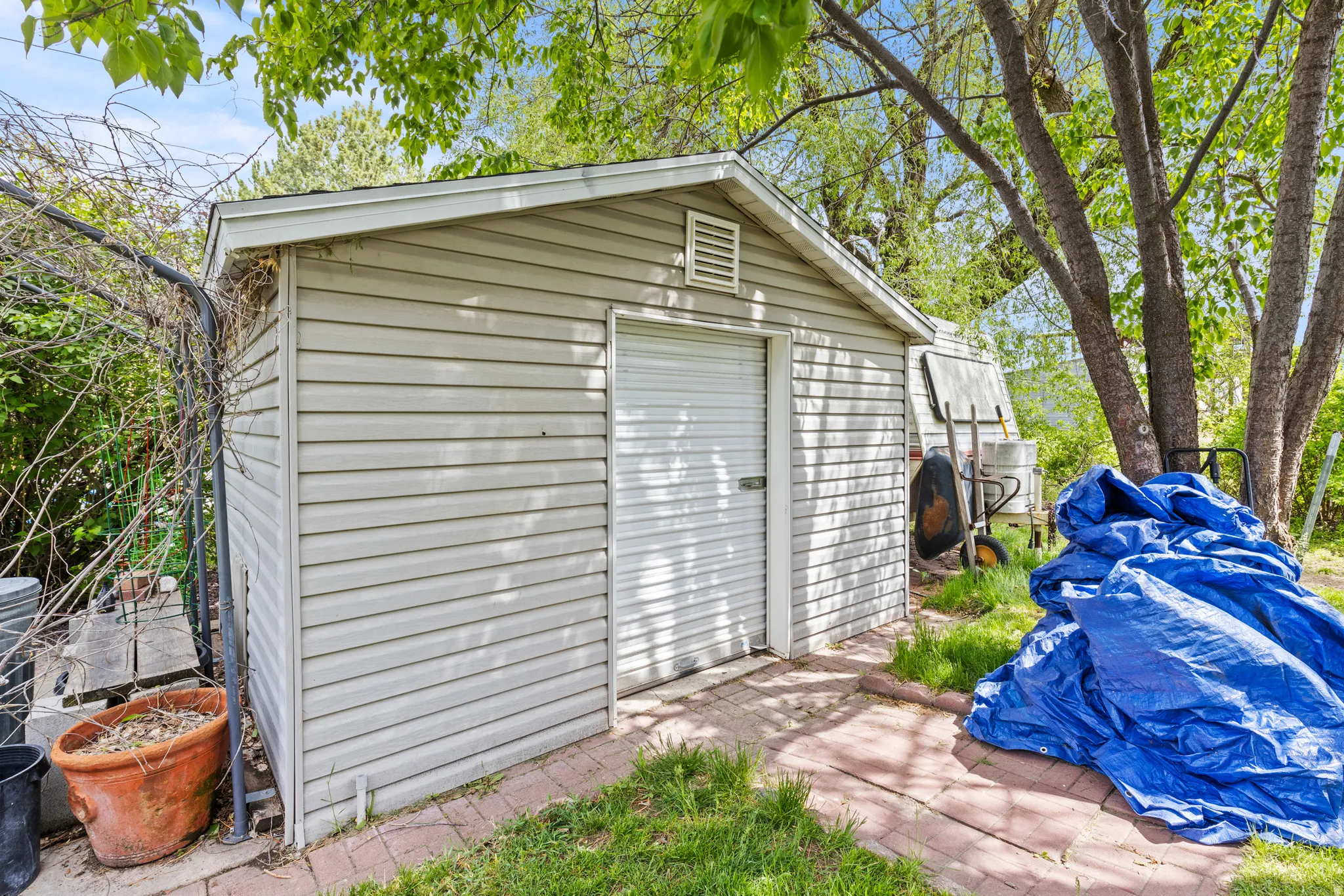 Outdoor storage shed with light-colored siding, a pitched roof, and a white roll-up door