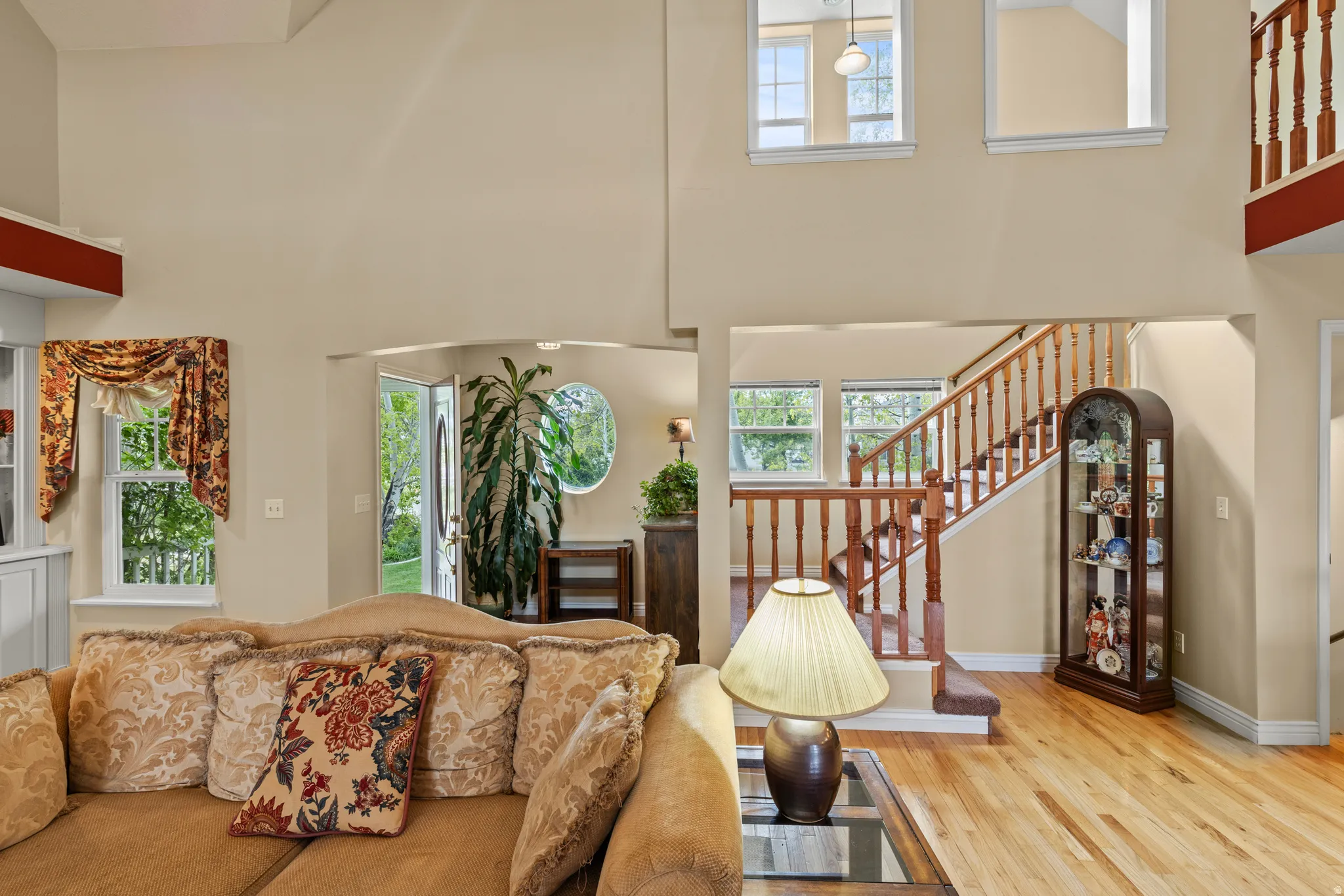 Vaulted ceiling with upper windows, hardwood flooring, and a natural wood staircase