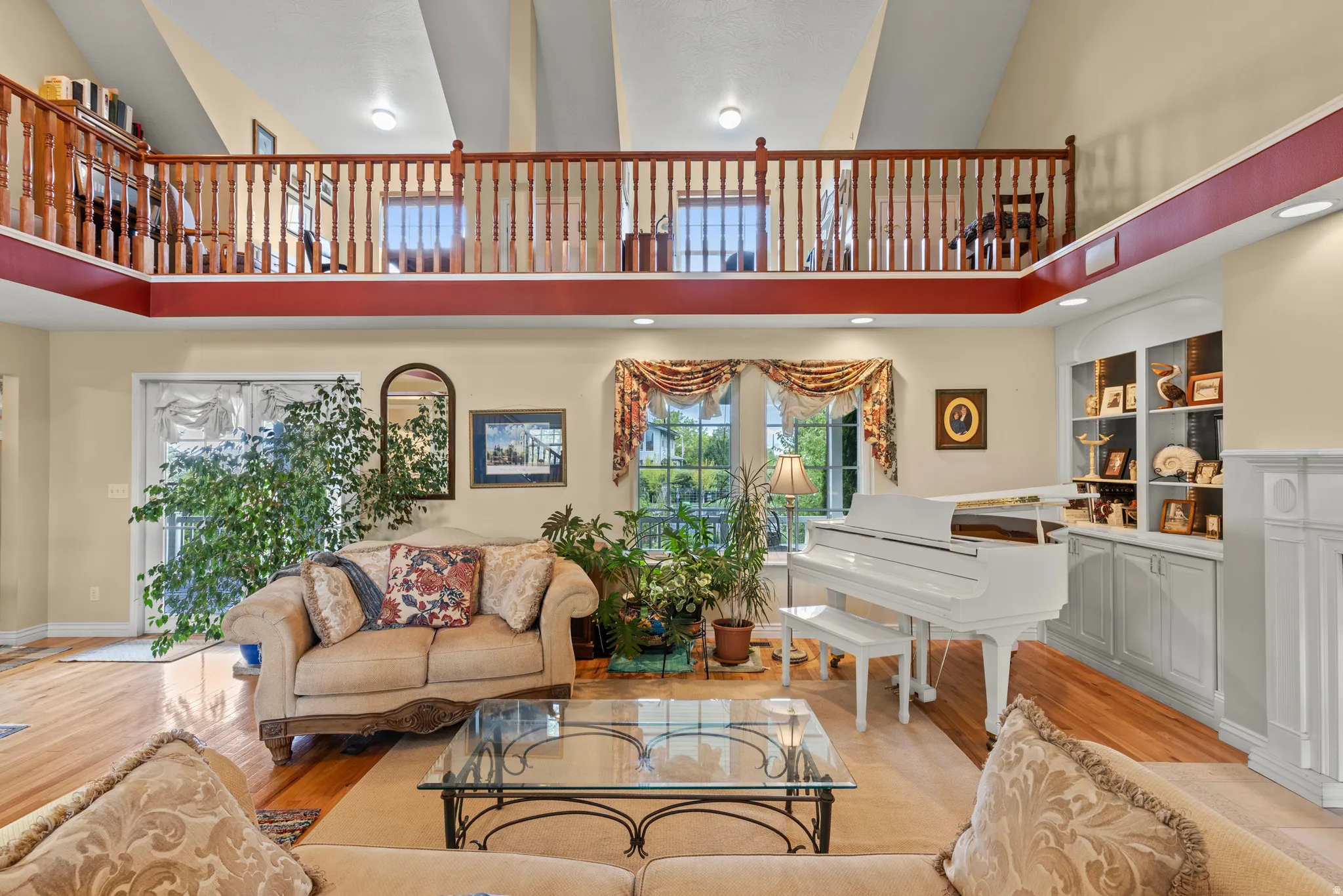 Living area featuring a high vaulted ceiling, hardwood flooring, an upper-level balcony with wood railings, built-in shelving, and a large window