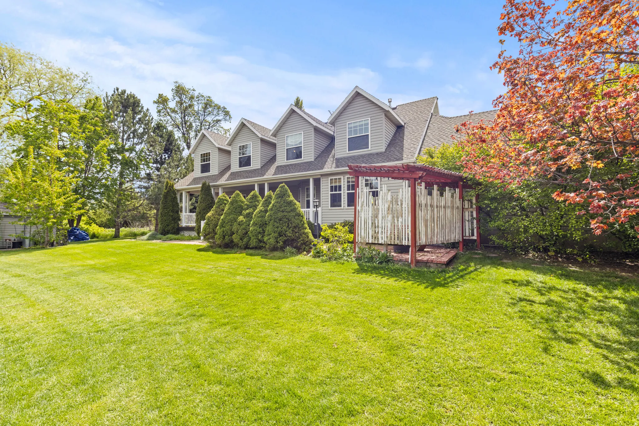 Expansive green lawn with a gray siding residence featuring multiple dormer windows and a covered front porch