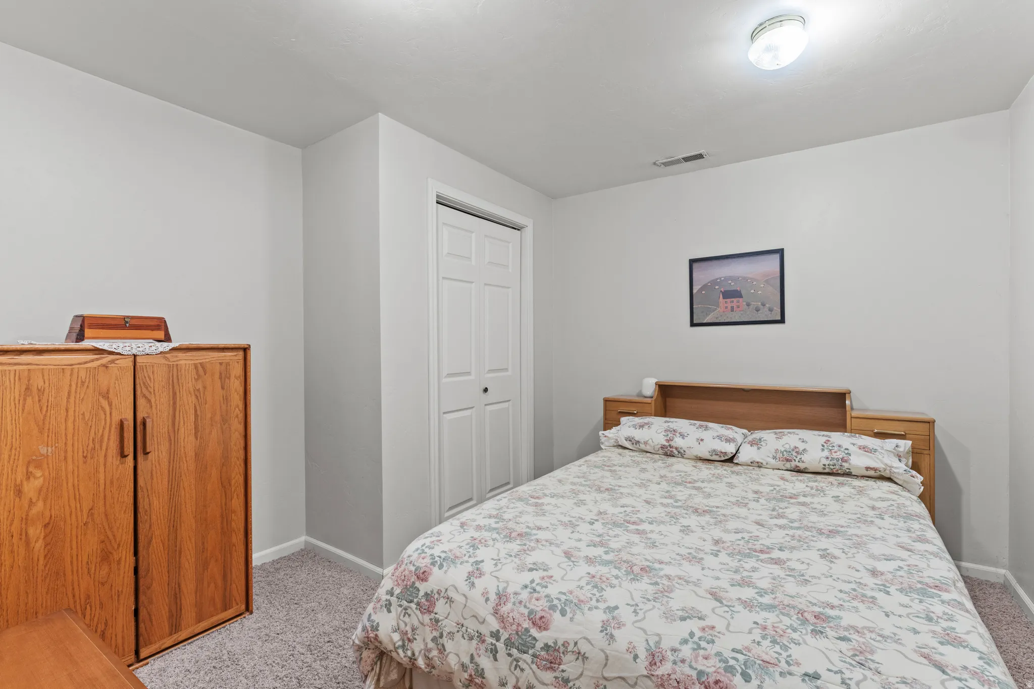 Carpeted room featuring light gray walls, a built-in closet with white bi-fold doors, and a ceiling-mounted light fixture