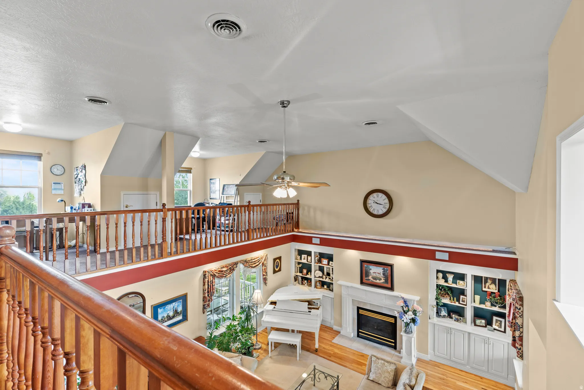 Vaulted ceilings enhance this open concept living area featuring a fireplace with a white mantle, built-in shelving, wood-finish flooring, and a second-story balcony with wood railings