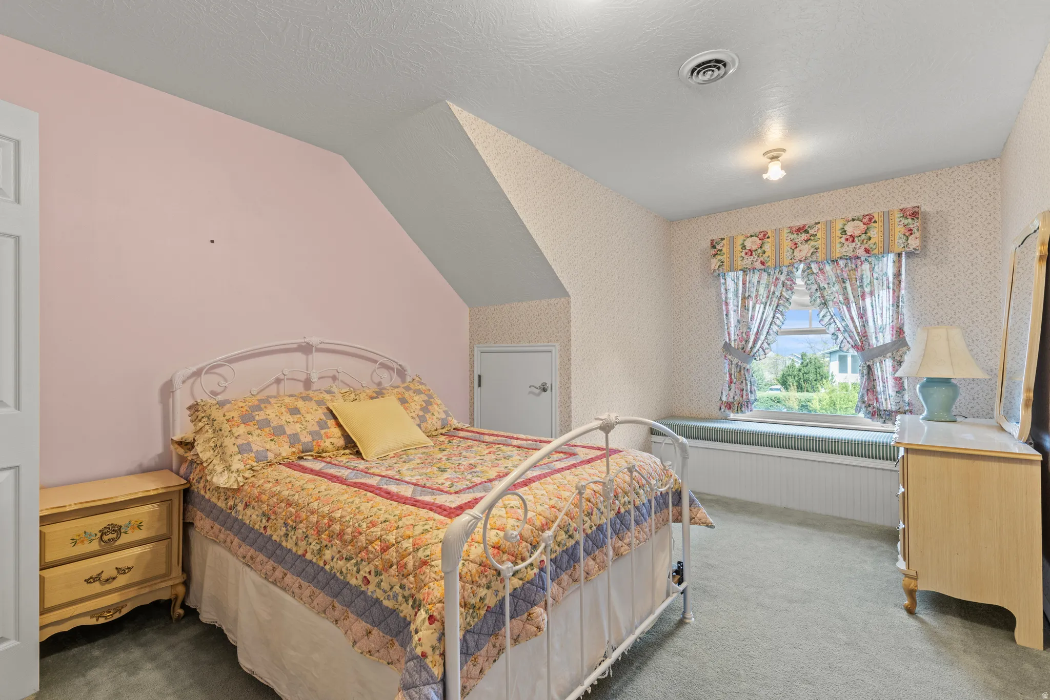 Room featuring an angled ceiling, a built-in window seat with storage, a large window, and patterned wallpaper
