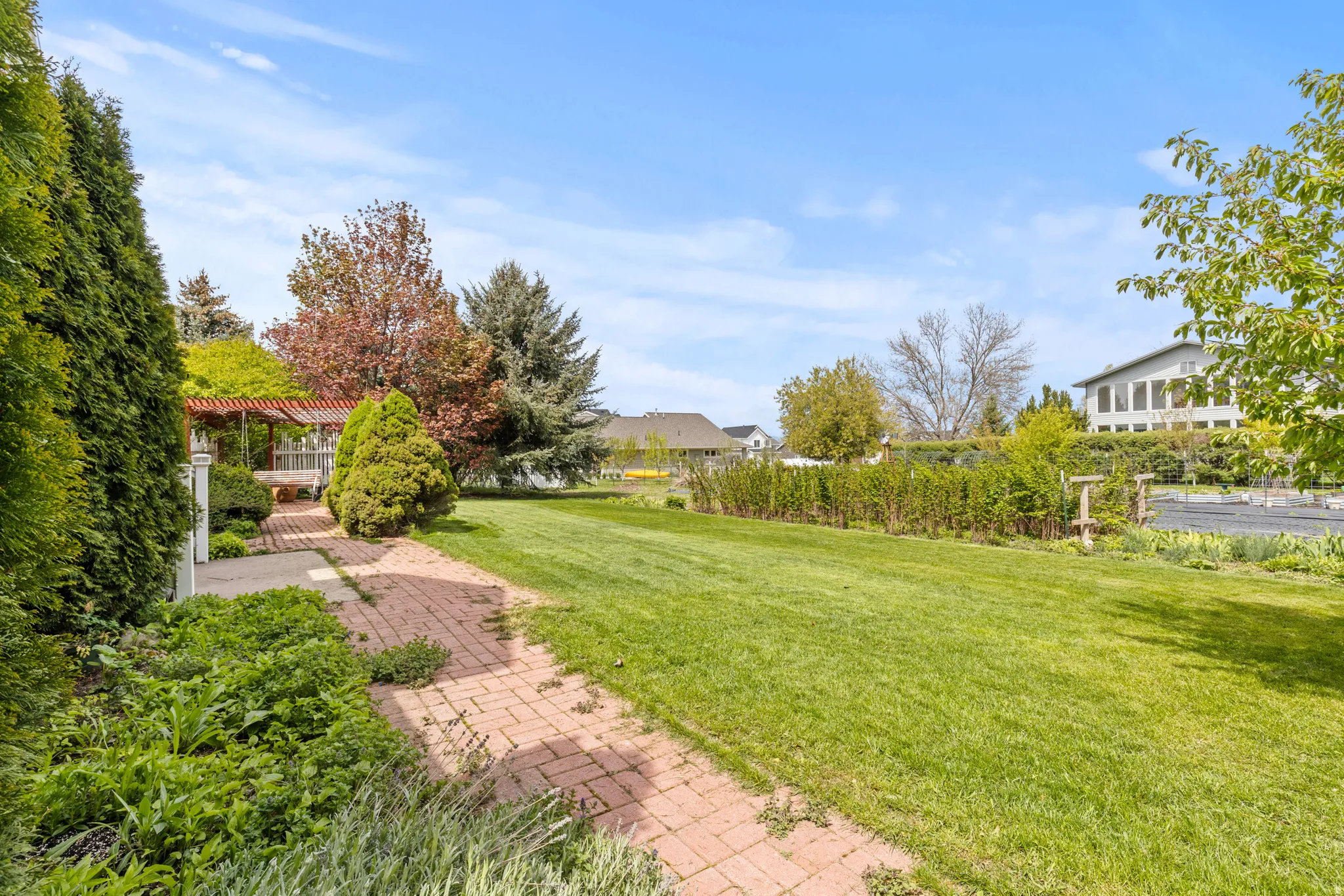 Expansive lawn area featuring a brick paver pathway, mature trees, and established perimeter landscaping