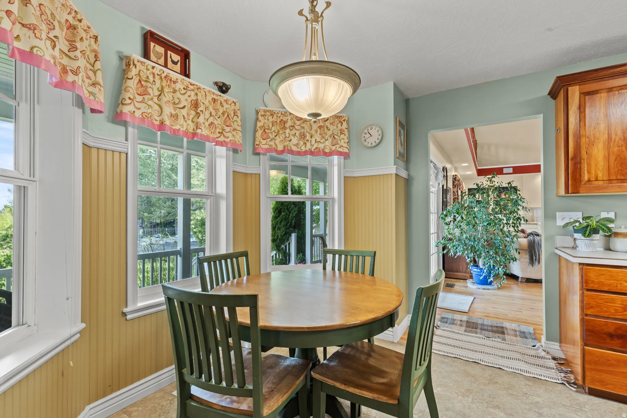 Bright dining area featuring beadboard wainscoting, multiple windows, a ceiling-mounted light fixture, and wood-finish cabinetry with a light-toned countertop