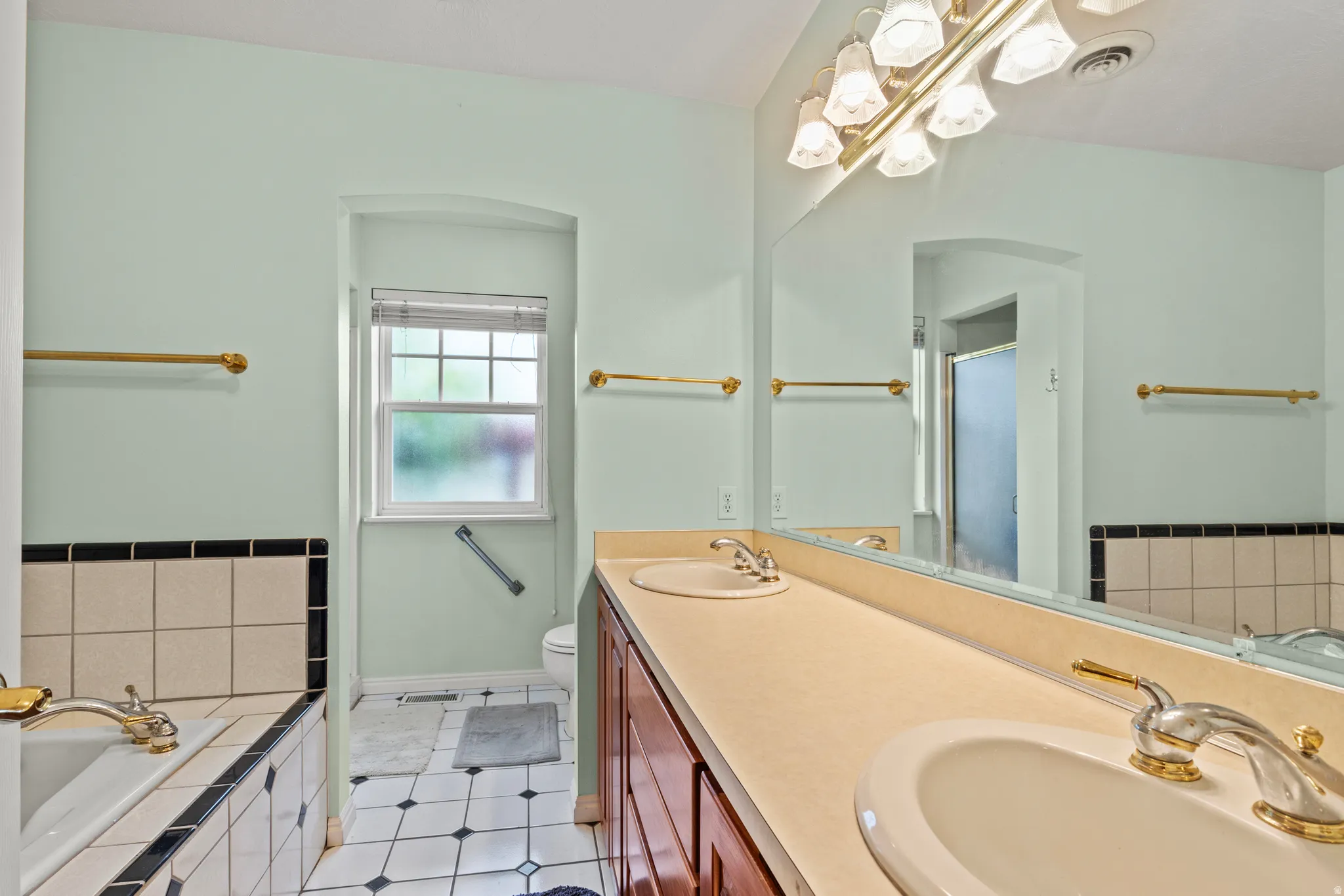 Bathroom featuring a dual vanity with integrated sinks, a large wall-mounted mirror, and a built-in bathtub with tiled surround