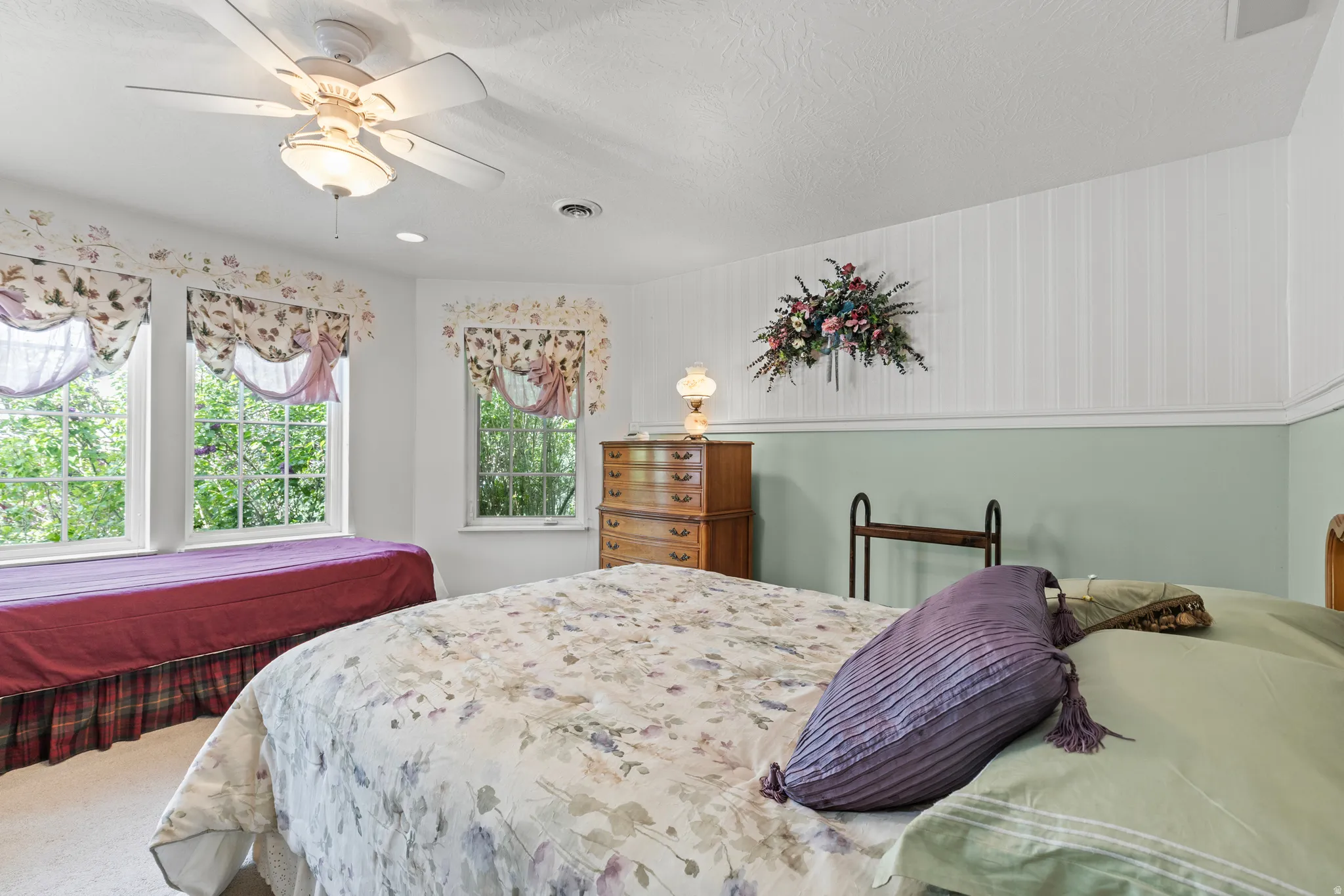 Room featuring a ceiling fan with integrated lighting, three windows with natural light, two-tone walls with wainscoting, and carpet flooring