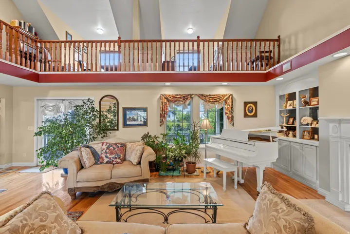 Living area featuring a high vaulted ceiling, hardwood flooring, an upper-level balcony with wood railings, built-in shelving, and a large window
