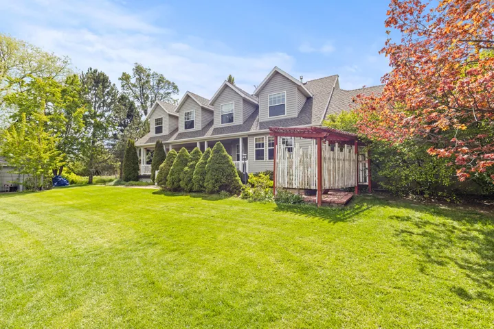 Expansive green lawn with a gray siding residence featuring multiple dormer windows and a covered front porch
