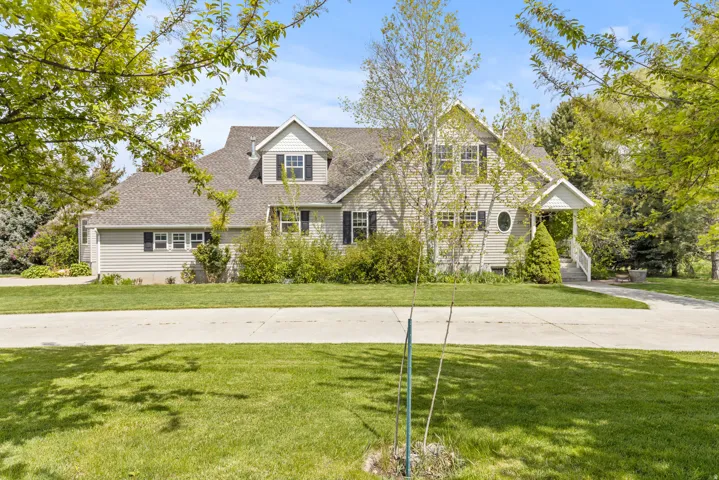 Two-story residence featuring light gray siding, dark shutters, a front porch with white railings, a circular window, and a gabled roofline