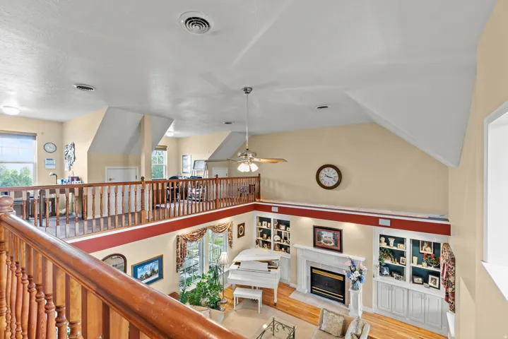 Vaulted ceilings enhance this open concept living area featuring a fireplace with a white mantle, built-in shelving, wood-finish flooring, and a second-story balcony with wood railings