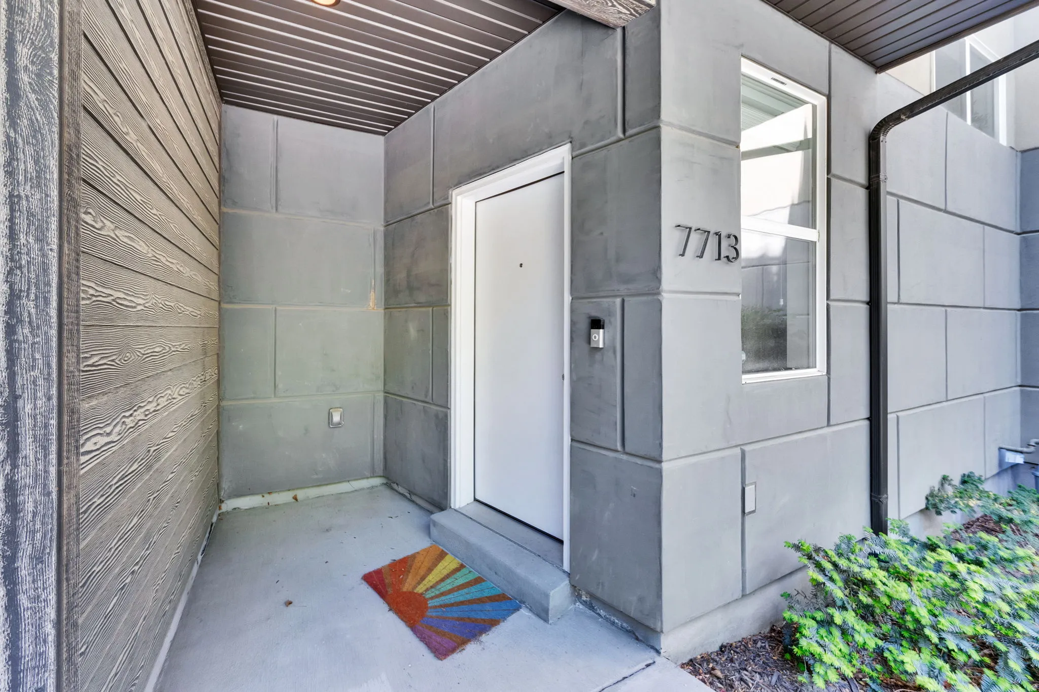 Modern entryway featuring a white door, contrasting gray siding, and a vertical window