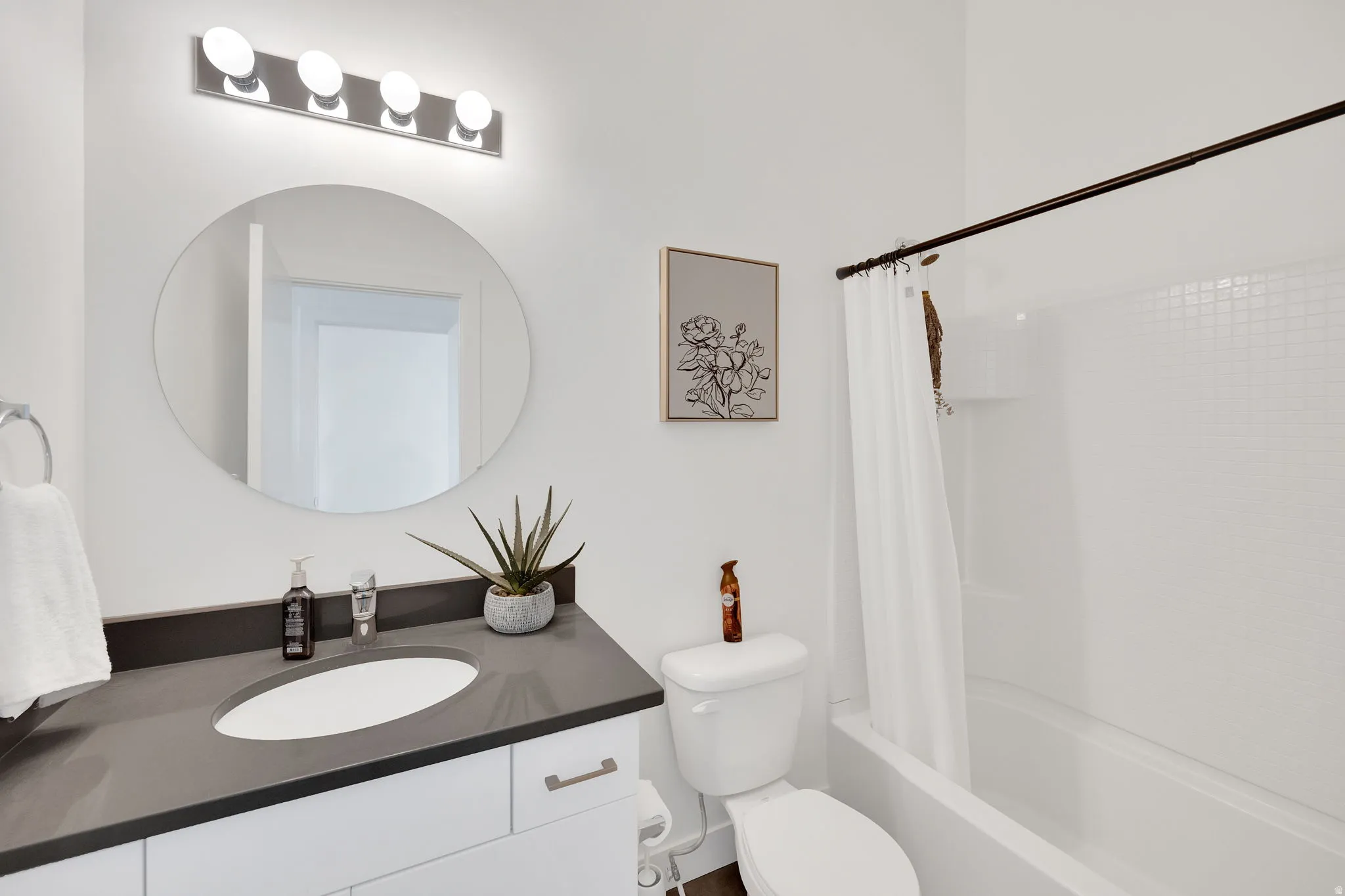 Bathroom featuring a white vanity with brushed nickel hardware, a dark countertop, an undermount sink, and a circular mirror