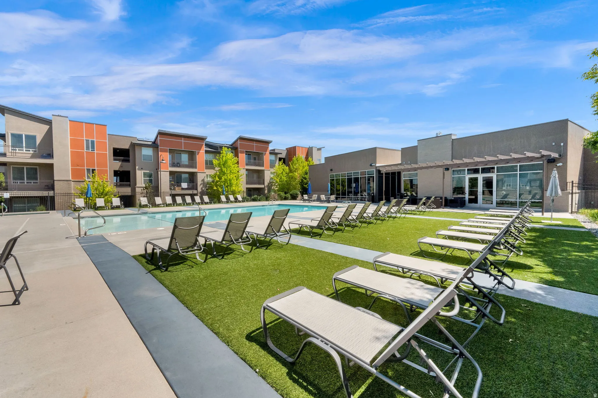 Expansive outdoor pool area featuring a rectangular swimming pool, surrounding concrete decking, and artificial turf lounge spaces