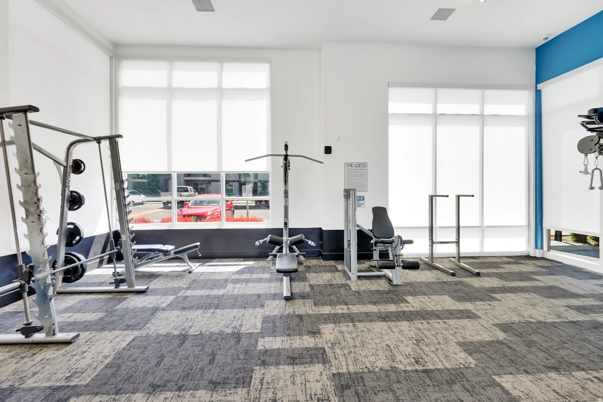 Fitness center with large windows, roller shades, high ceilings, and patterned carpet tile flooring