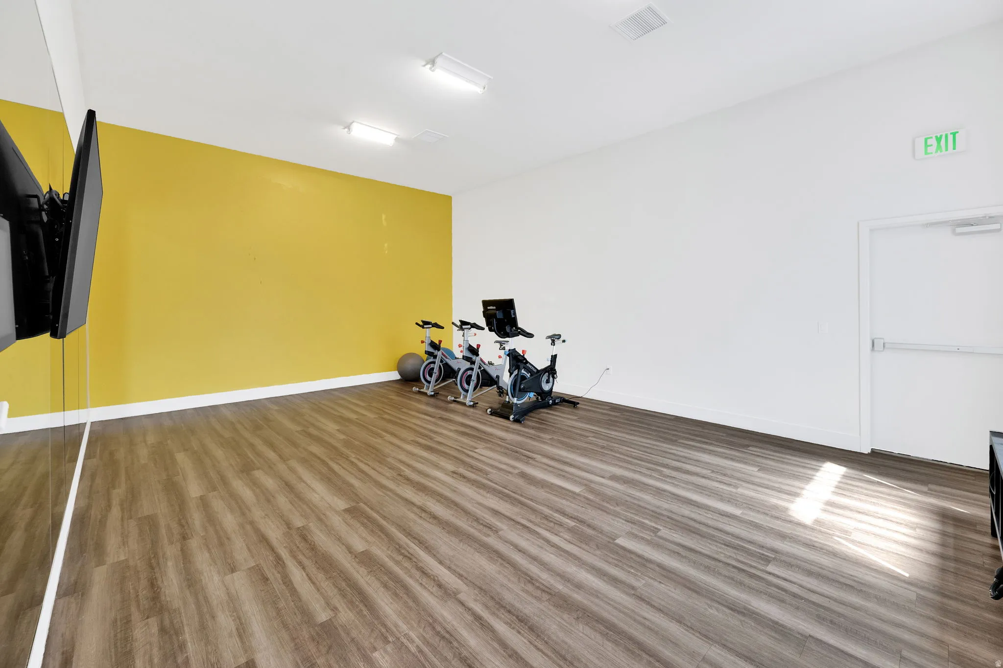 Spacious room featuring wood-finish flooring, a full mirrored wall, and a vibrant accent wall