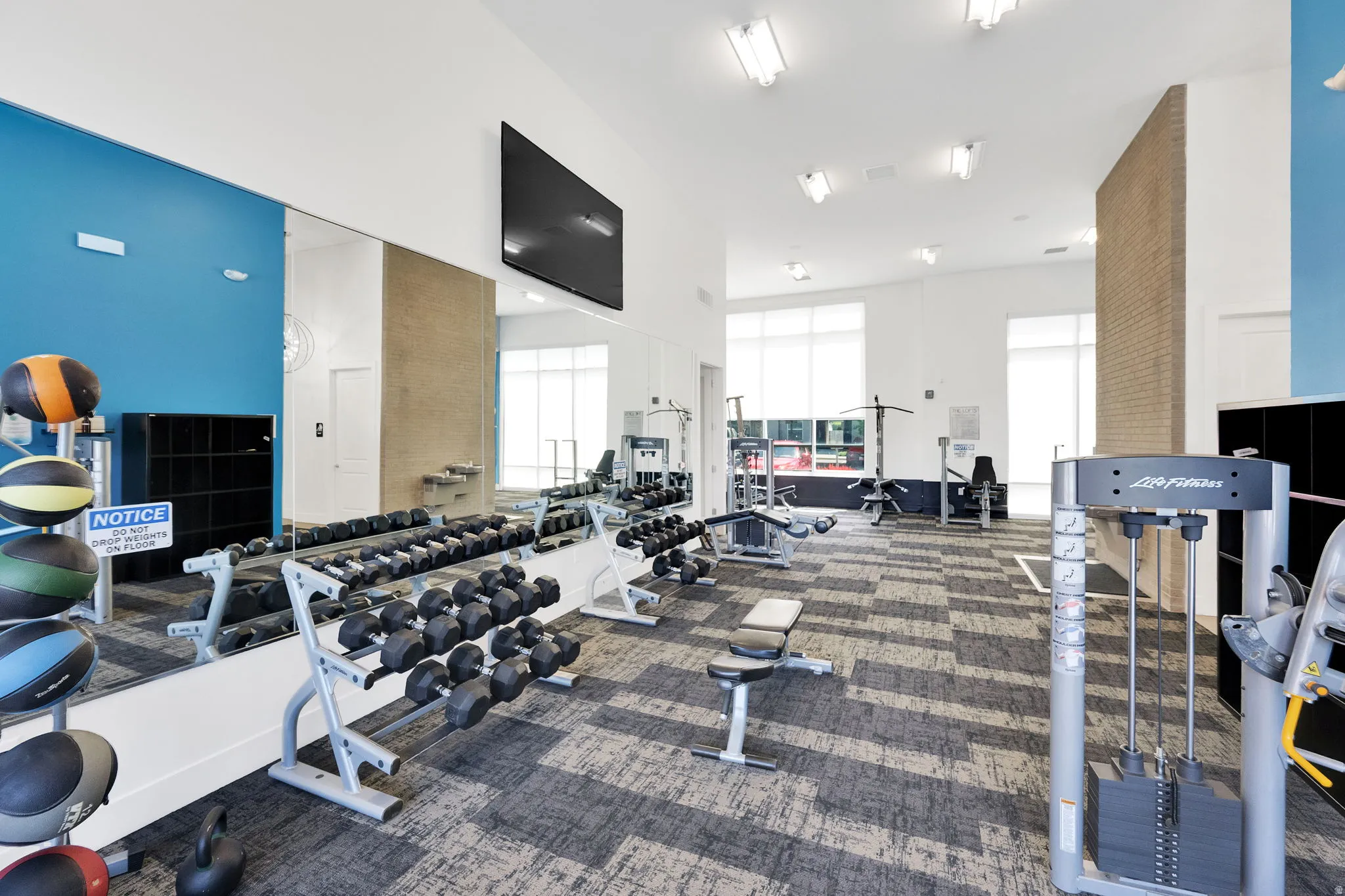 Fitness center featuring extensive mirrored walls, a mounted flat-screen display, high ceilings with flush lighting, and large windows with privacy blinds