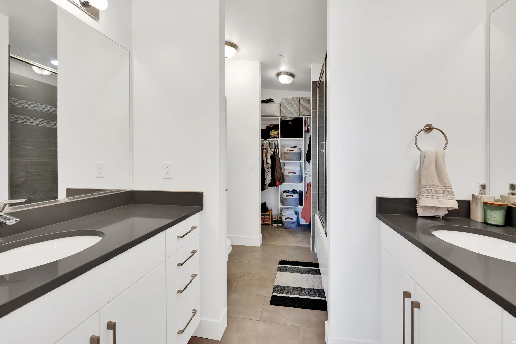 Bathroom featuring dual vanities with dark countertops, white cabinetry, and undermount sinks