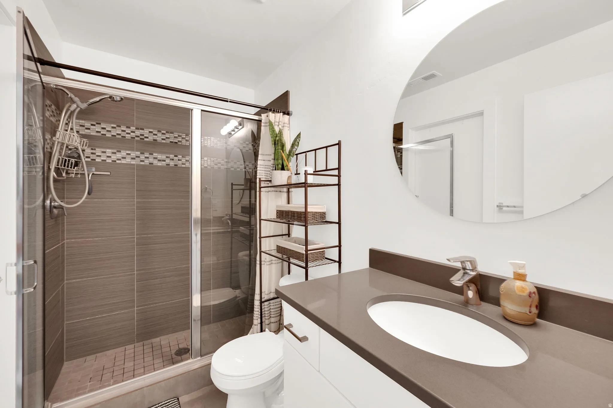Modern bathroom featuring a glass-enclosed shower with gray tile surround and mosaic accent