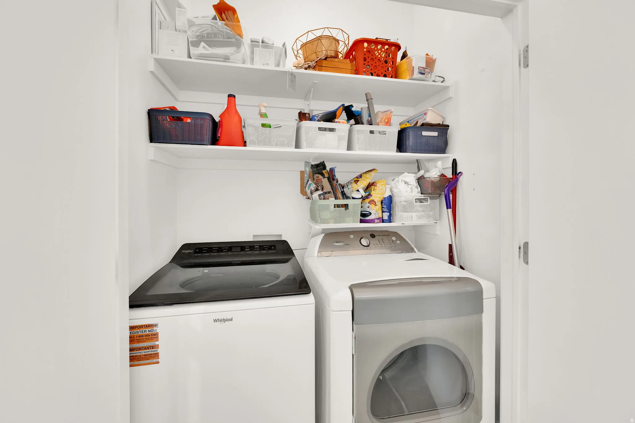 Laundry closet featuring a top-load washing machine, front-load dryer, and multiple overhead shelving units