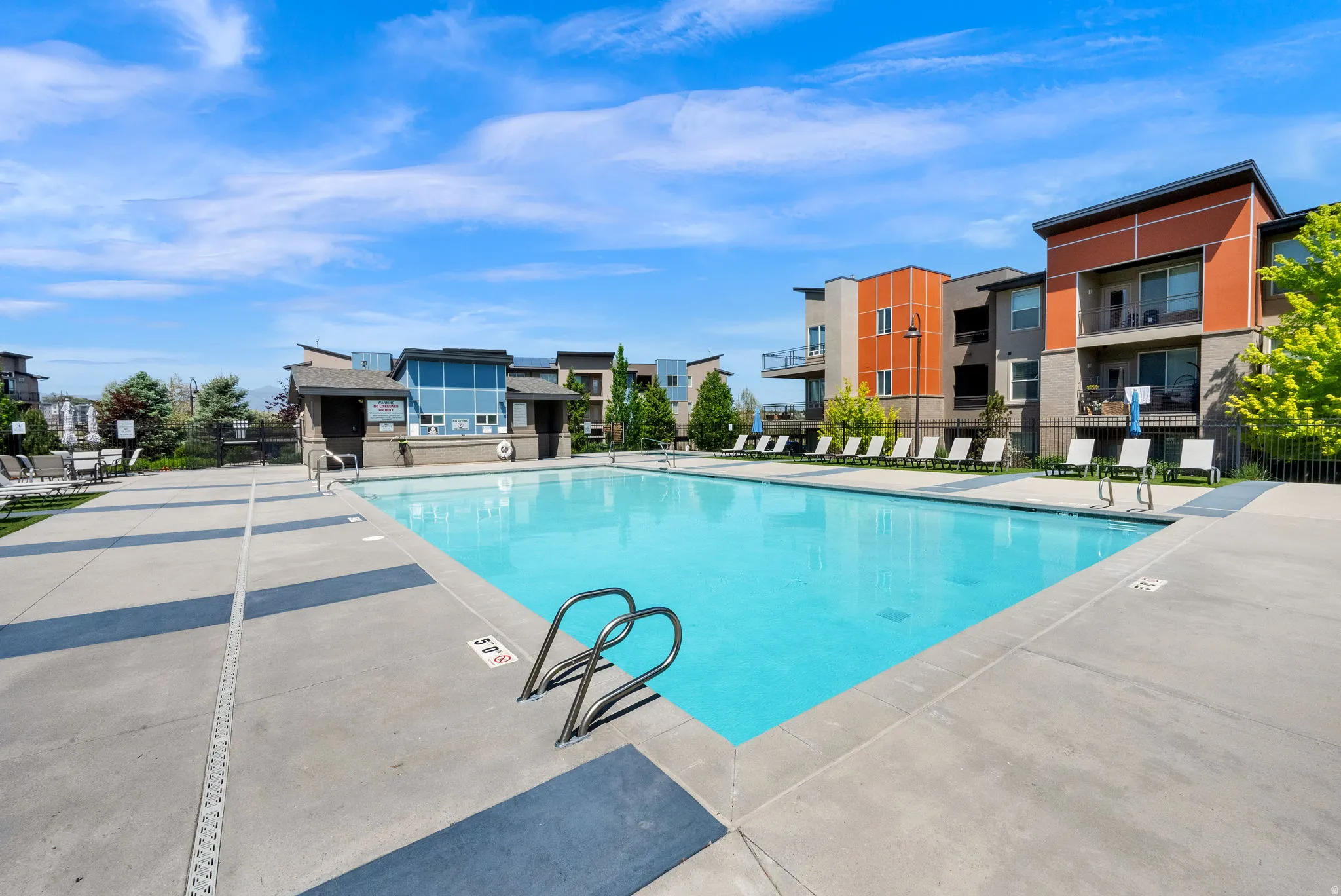 Outdoor swimming pool with concrete decking, surrounded by multiple modern residential buildings featuring balconies