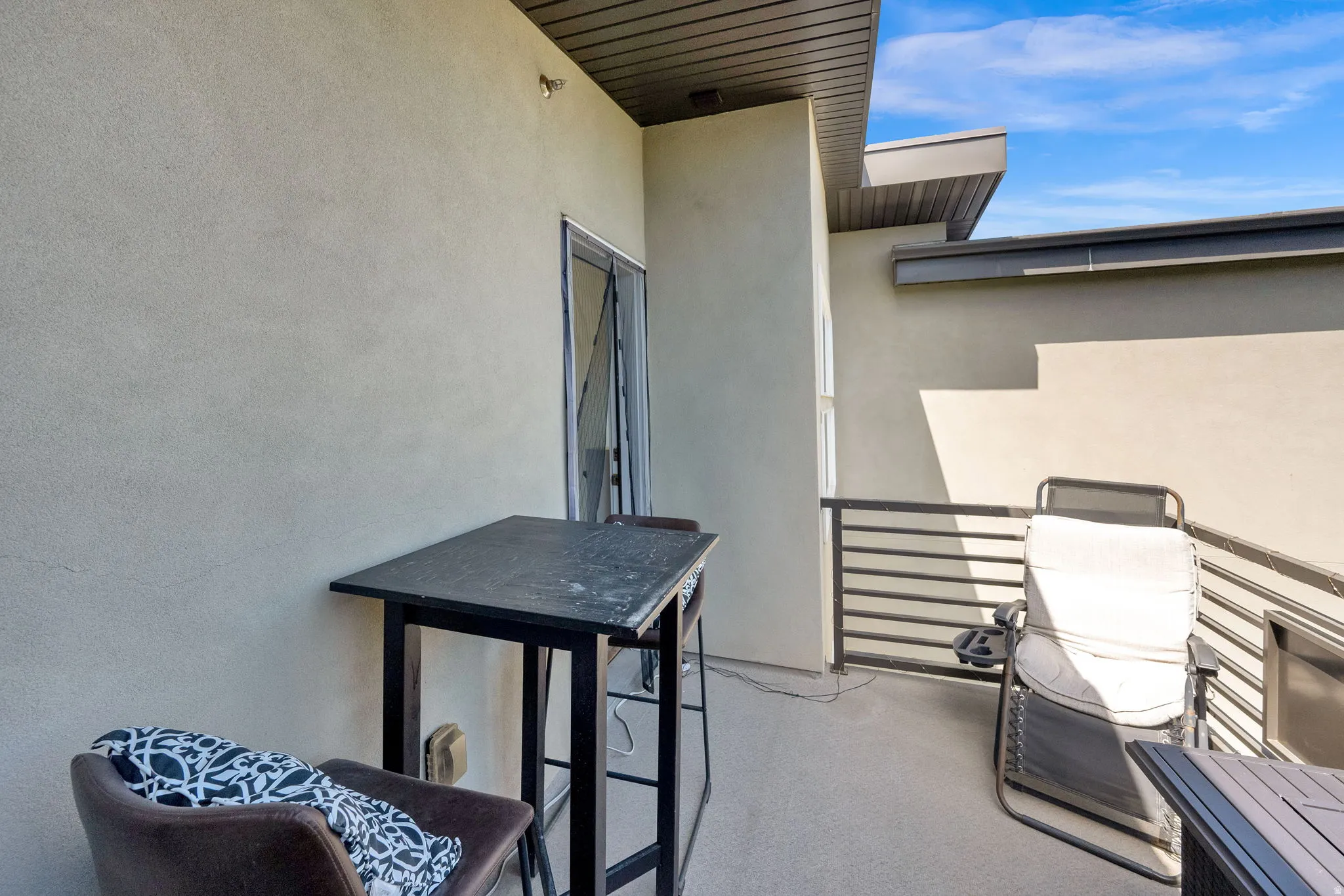 Private outdoor patio featuring a textured stucco exterior, a sliding glass door, and metal horizontal railings