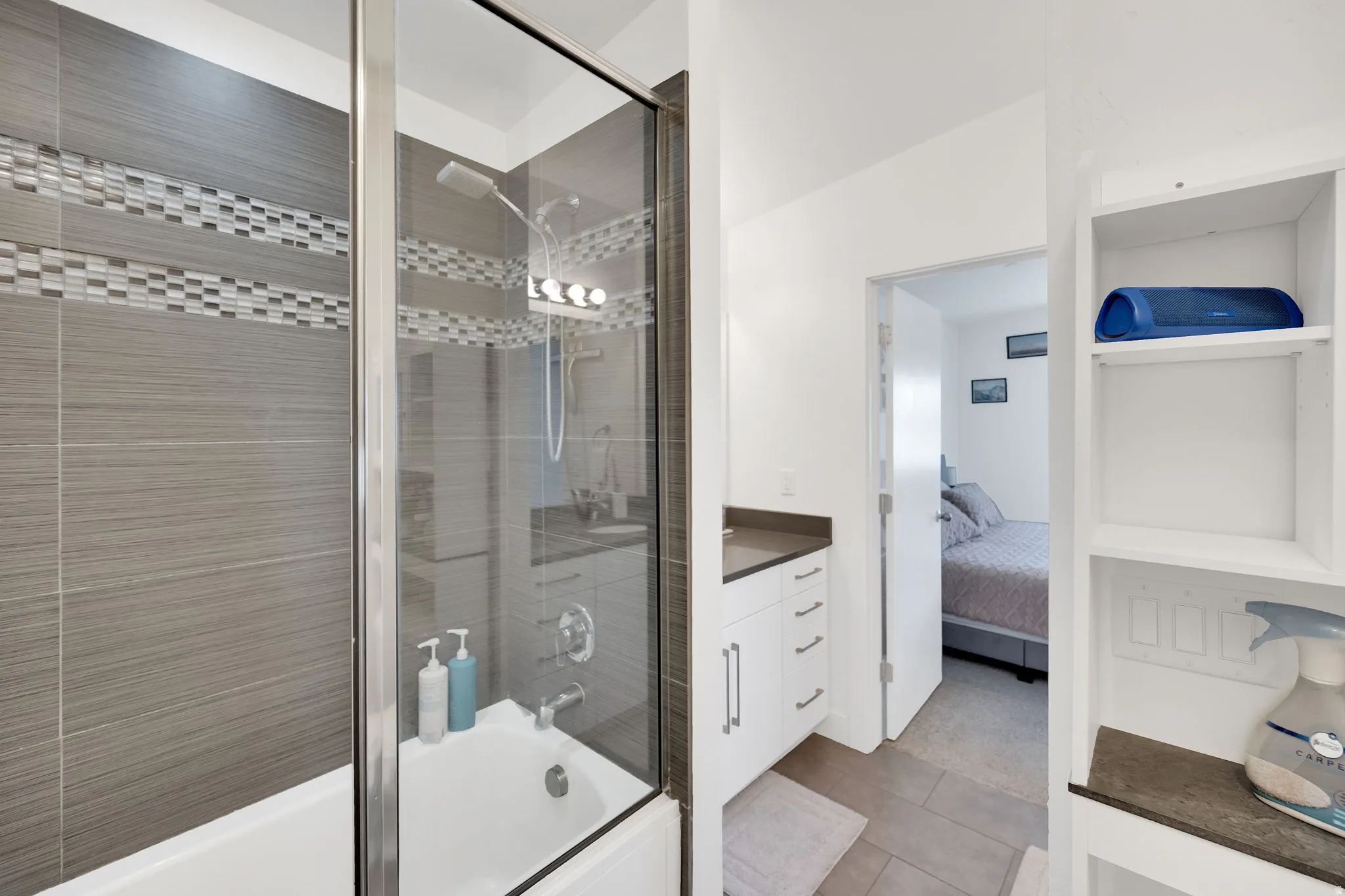 Bathroom featuring a tiled shower with glass enclosure, white bathtub, vanity with white cabinetry, and built-in shelving