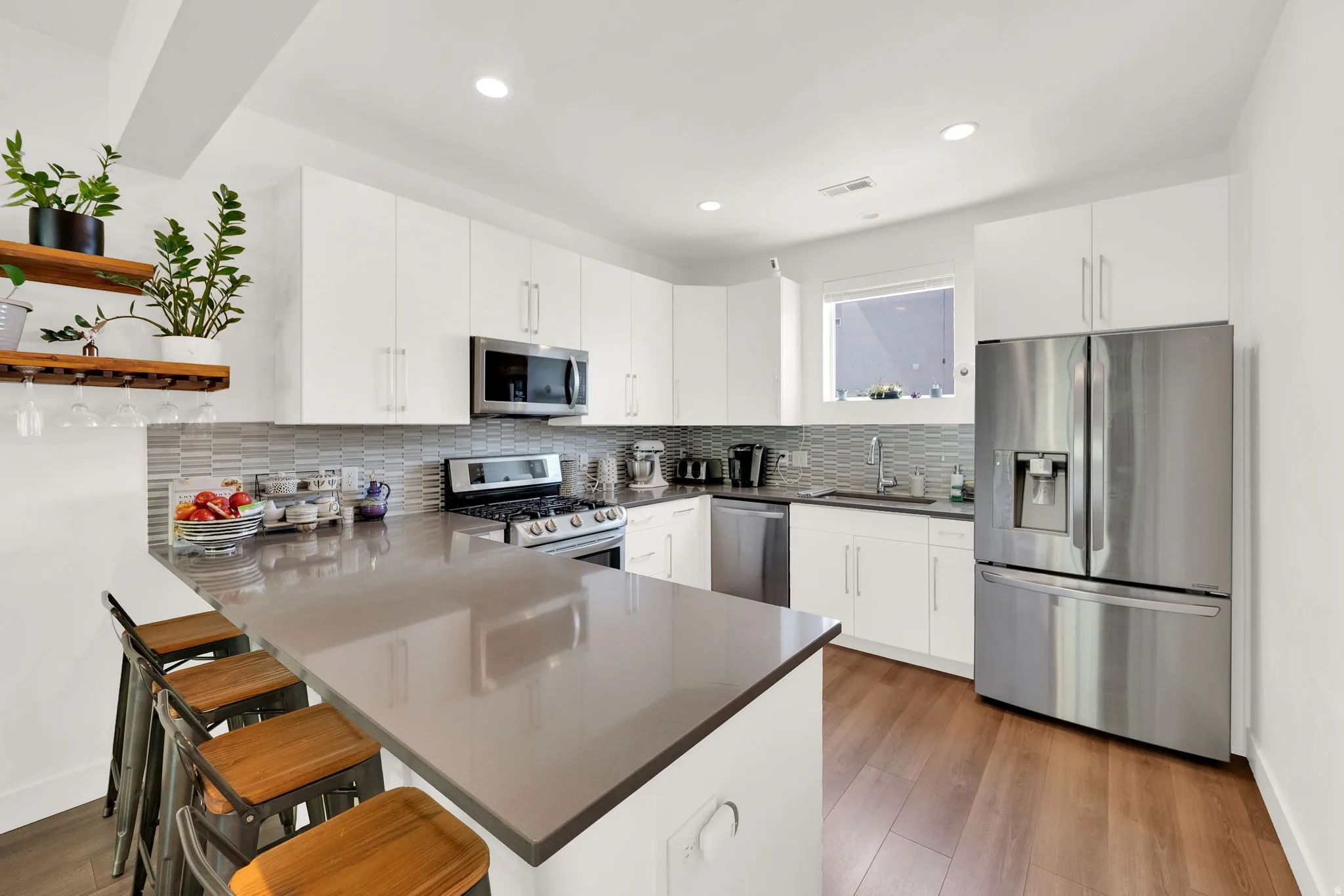 Kitchen featuring a peninsula with countertop seating, stainless steel appliances, wood-finish flooring, white cabinetry, and a subway tile backsplash
