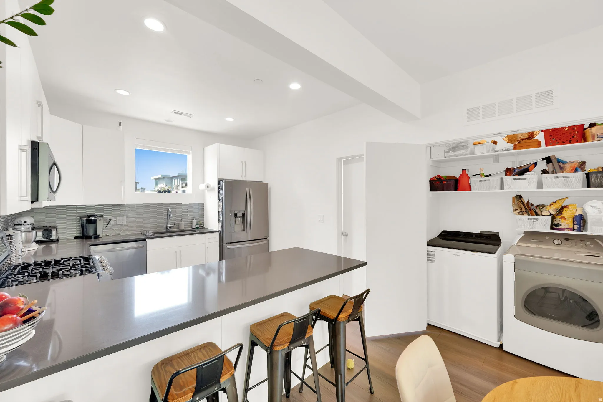 Modern kitchen featuring white cabinetry, stainless steel appliances, a grey countertop island, and wood-finish flooring
