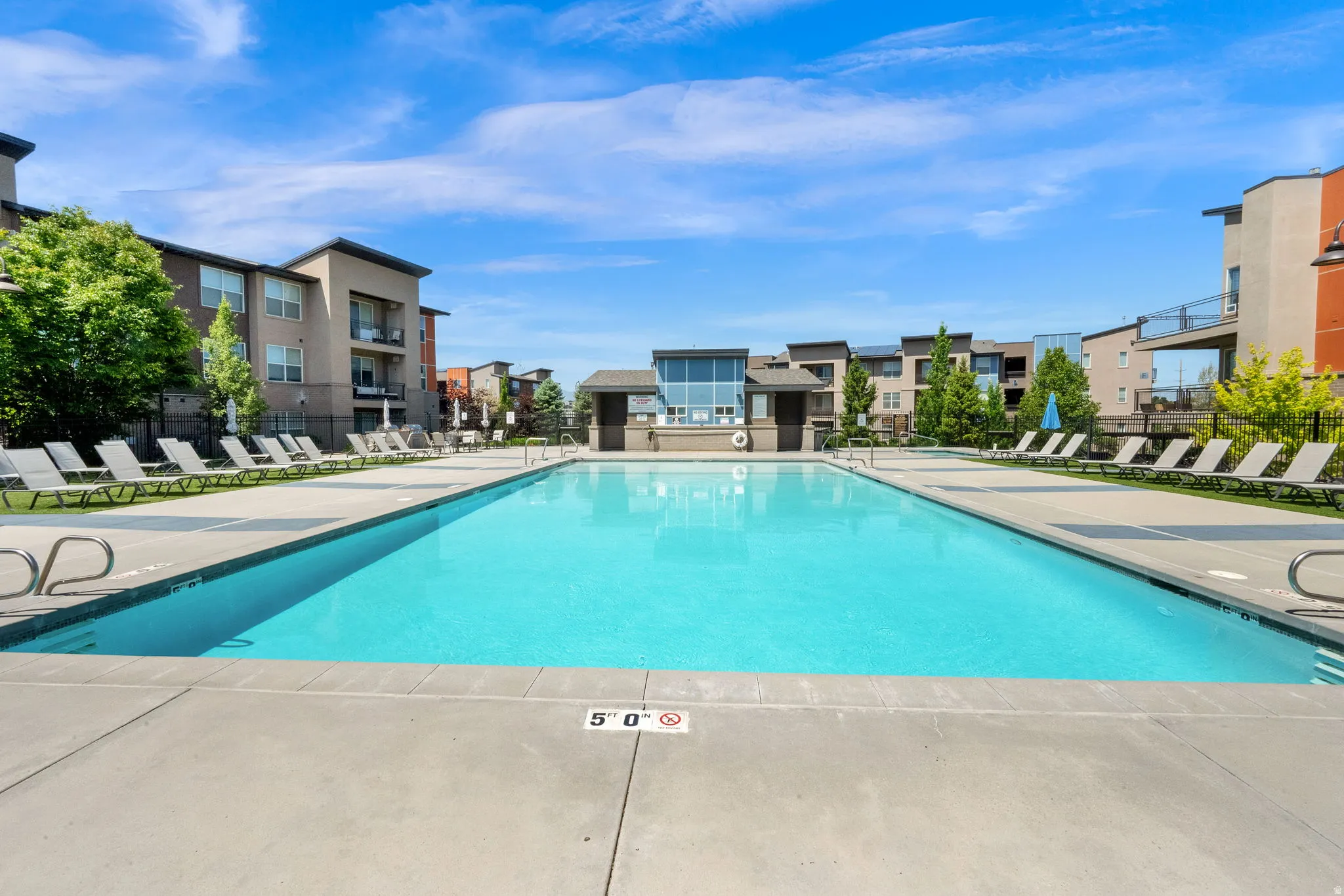 Expansive outdoor swimming pool with surrounding concrete decking, multiple lounge chairs, and a contemporary architectural building in the background